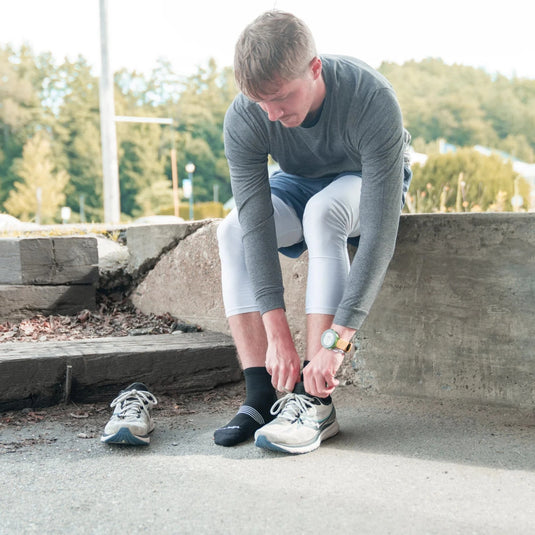 Man tying his running shoes outdoors with trees in the background