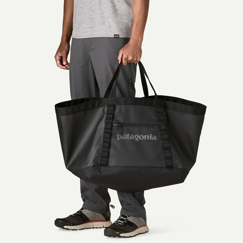 Load image into Gallery viewer, Person holding a black Patagonia tote bag on a white background