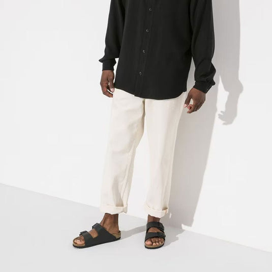 Person wearing a black shirt, white pants, and black sandals on a white background