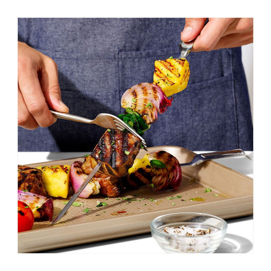 Person holding a skewer of grilled vegetables and meat with a blue apron in the background.