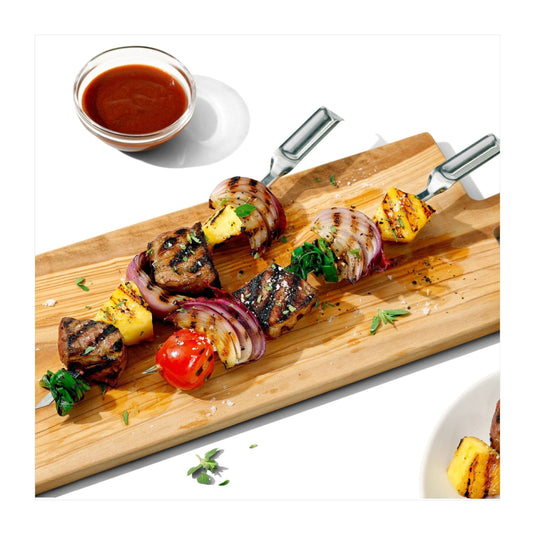 Grilled skewers with vegetables on a wooden board with a small bowl of sauce.