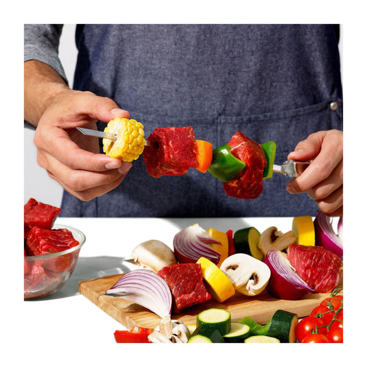 Person preparing a skewer with vegetables and meat on a cutting board.