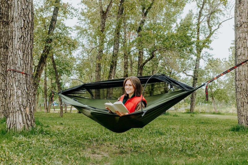 Load image into Gallery viewer, Hammock with mosquito net in a wooded area, person relaxing while reading.