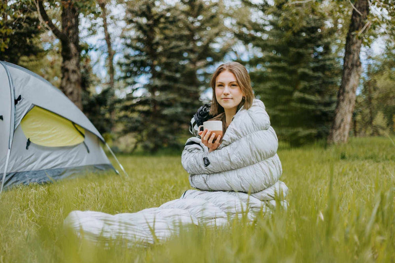 Load image into Gallery viewer, Outdoor camping scene with person in Goose Down Sleeping Bag Grey near a tent.