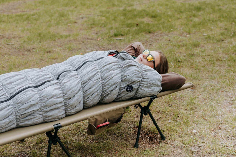 Load image into Gallery viewer, Grey goose down sleeping bag on a portable camping bed outdoors.