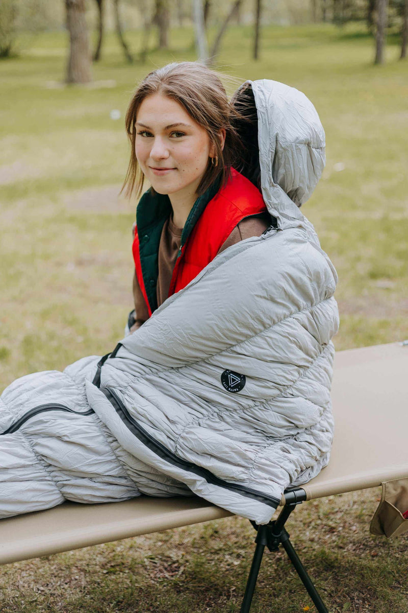 Load image into Gallery viewer, Grey goose down sleeping bag with person sitting inside, showcasing warmth and comfort for outdoor use.