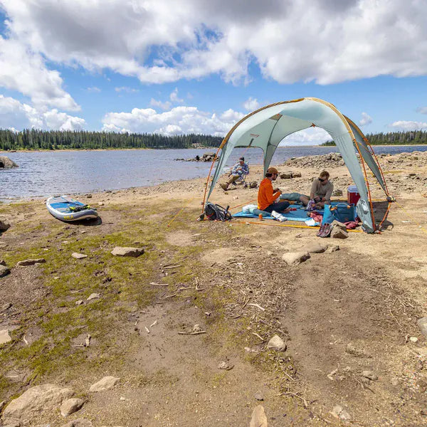 Load image into Gallery viewer, Two people sitting under a tent by a lake with a kayak nearby.