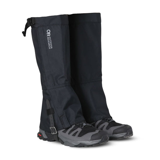 Black gaiters attached to gray hiking boots on a white background