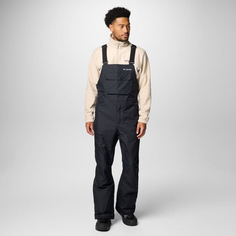 Load image into Gallery viewer, Person wearing black bib overalls with a beige jacket on a white background