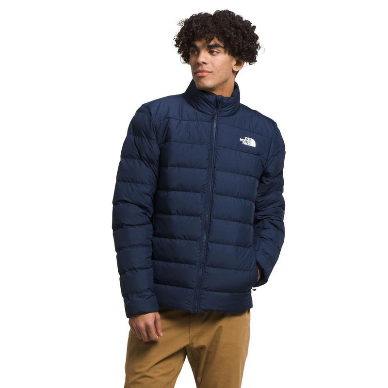 Load image into Gallery viewer, Person wearing a navy blue puffer jacket with a brand logo on a white background