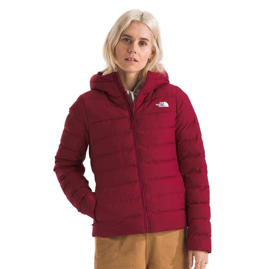 A woman wearing a red The North Face Women's Aconcagua 3 Hoodie with a hood, zippered front, and handwarmer pockets.