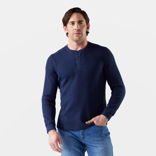 Man wearing a navy blue long-sleeve henley shirt and jeans on a light gray background