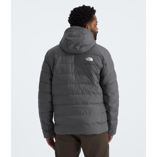Person wearing a gray puffer jacket with a visible brand logo on a white background