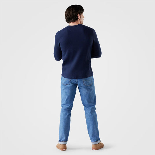 Person wearing a navy sweater and blue jeans on a light gray background