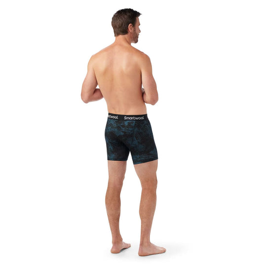 Man wearing black patterned boxer briefs with 'Smartwool' branding on a white background
