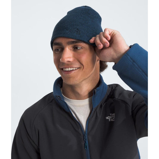 Person wearing a navy beanie and black jacket with The North Face logo on a white background