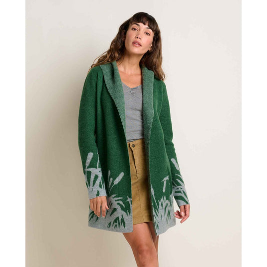 Woman wearing a green cardigan with leaf pattern on a plain background