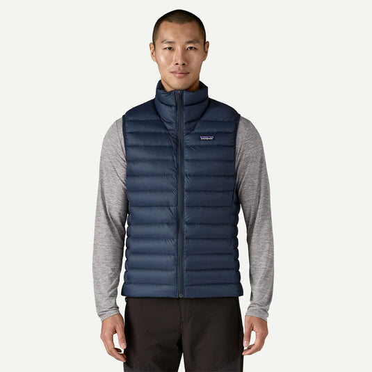 Man wearing a blue puffer vest over a gray shirt on a white background