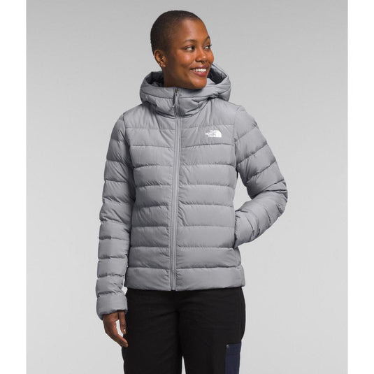 Woman wearing a gray puffer jacket with a visible brand logo on a light gray background