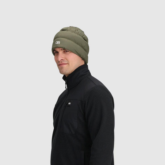 Man wearing a green beanie with a logo on a light gray background