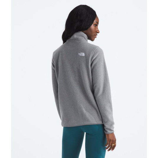 Woman wearing a gray fleece jacket with a brand logo on the back, standing against a white background.