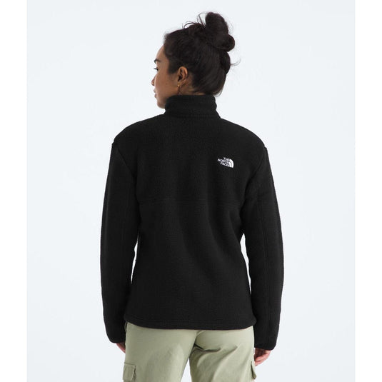 Person wearing a black fleece jacket with a logo on the back, standing against a white background