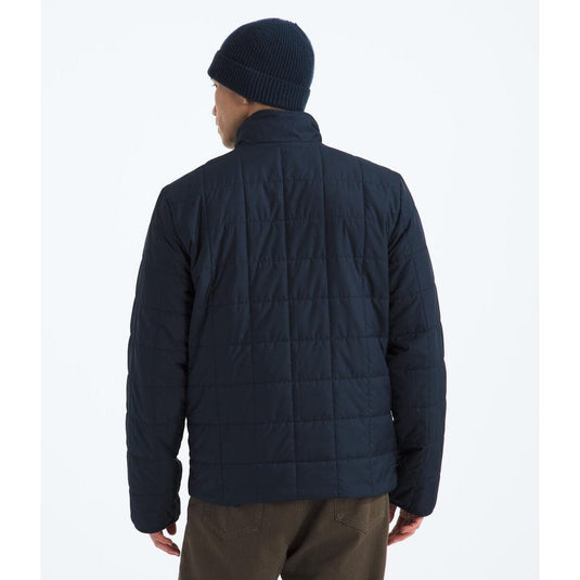 Person wearing a dark blue quilted jacket and beanie on a white background