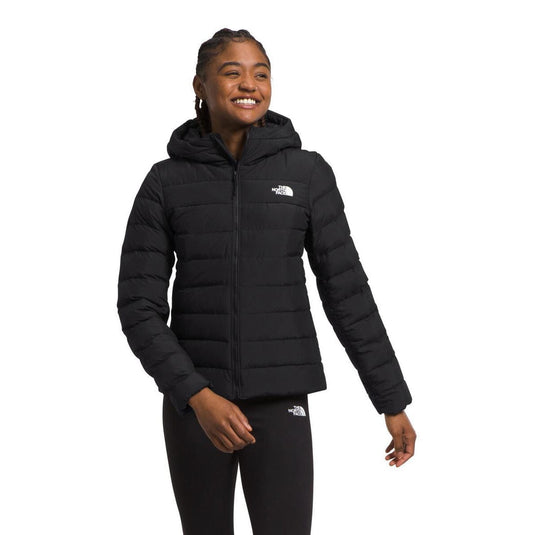 A woman wearing a red The North Face Women's Aconcagua 3 Hoodie with a hood, zippered front, and handwarmer pockets.