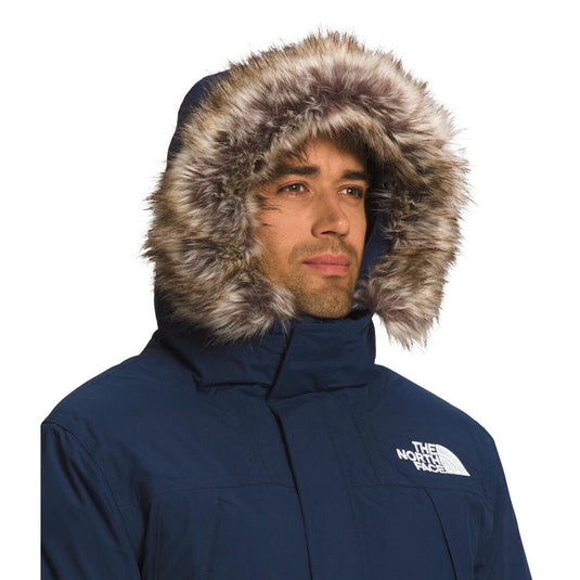 Man wearing a navy blue winter jacket with a fur-lined hood on a white background