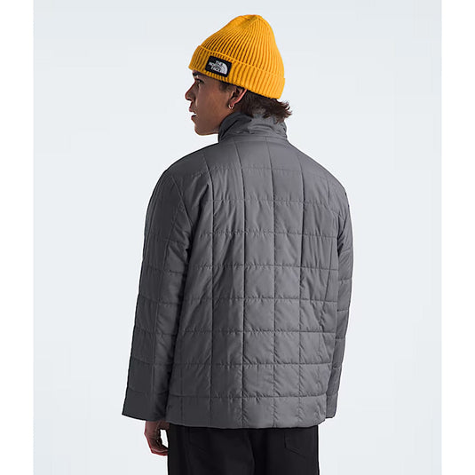 Person wearing a gray quilted jacket and yellow beanie on a white background