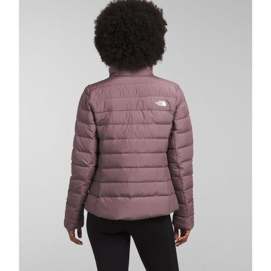 Person wearing a purple puffer jacket with a brand logo on a gray background