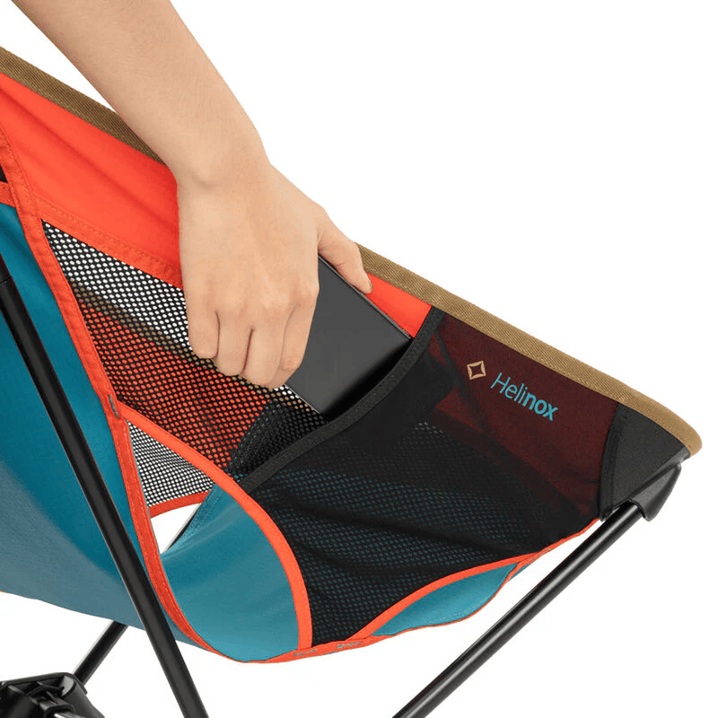 Load image into Gallery viewer, Colorful camping chair with a hand holding a black device, branded 'Helinox'.