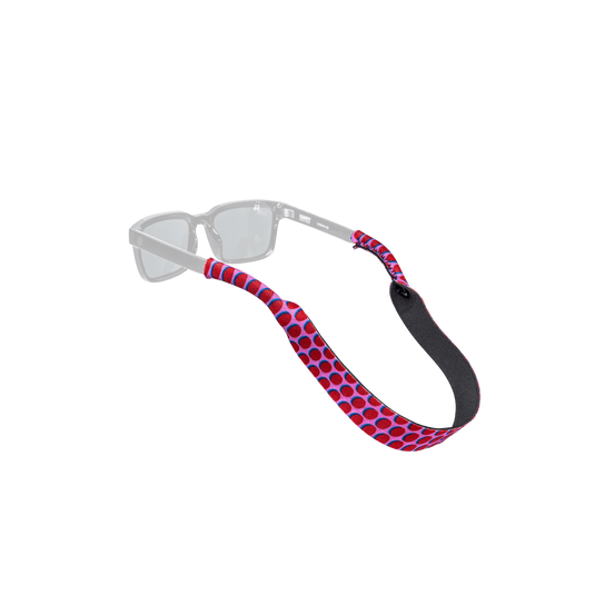 A pair of clear-framed sunglasses with a red and blue polka dot patterned strap, shown against a solid white background.