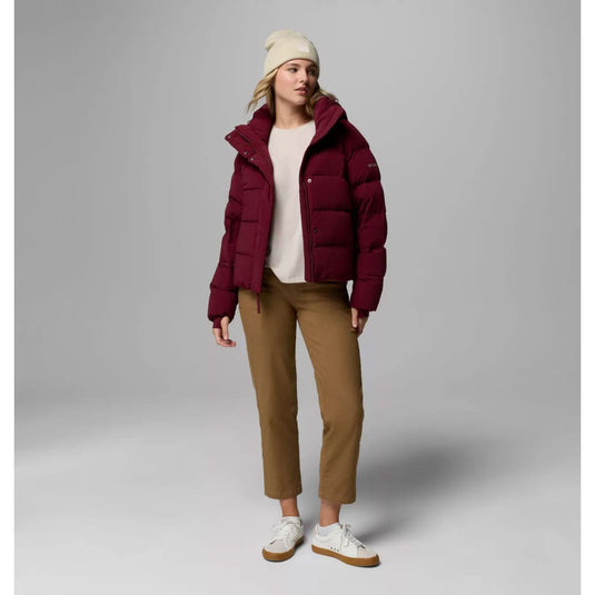 Person wearing a burgundy puffer jacket, beige beanie, white shirt, brown pants, and white sneakers on a gray background