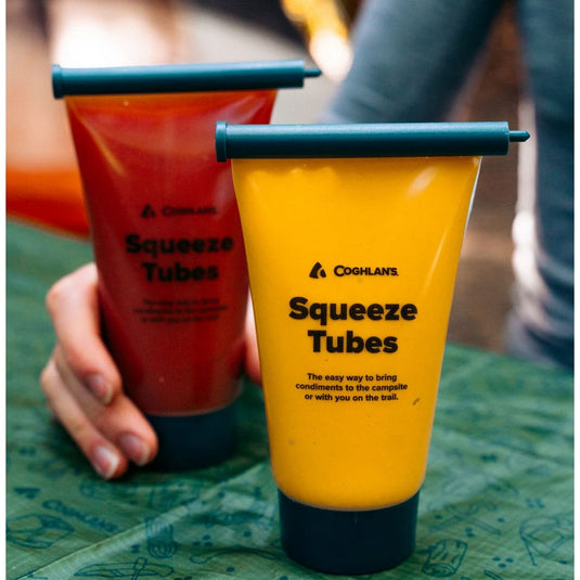 Two Coghlans Squeeze Tubes, one red and one yellow, on a green surface.