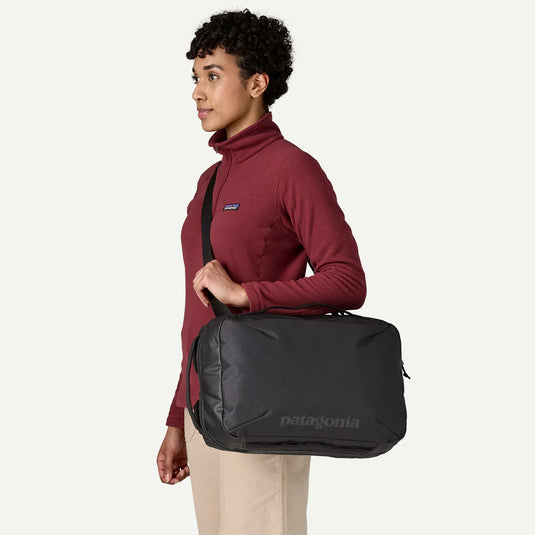 Person wearing a maroon jacket with a Patagonia logo, holding a black patagonia duffel bag on a white background