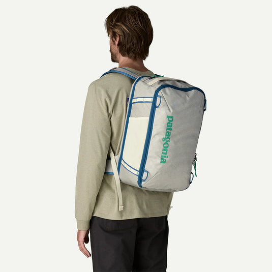 Person wearing a white Patagonia backpack with blue trim on a plain background