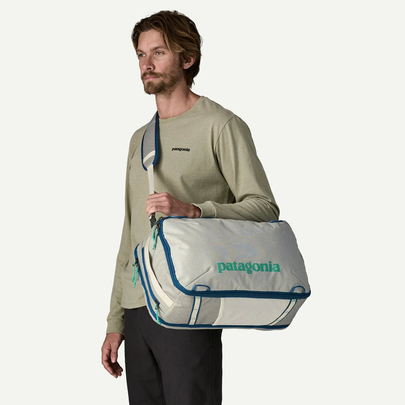 Load image into Gallery viewer, Man holding a white Patagonia duffel bag with blue trim against a white background
