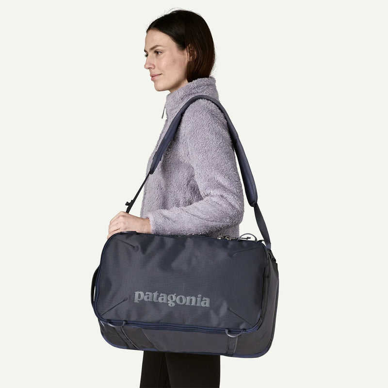Load image into Gallery viewer, Woman carrying a navy and grey Patagonia duffel bag on a white background

