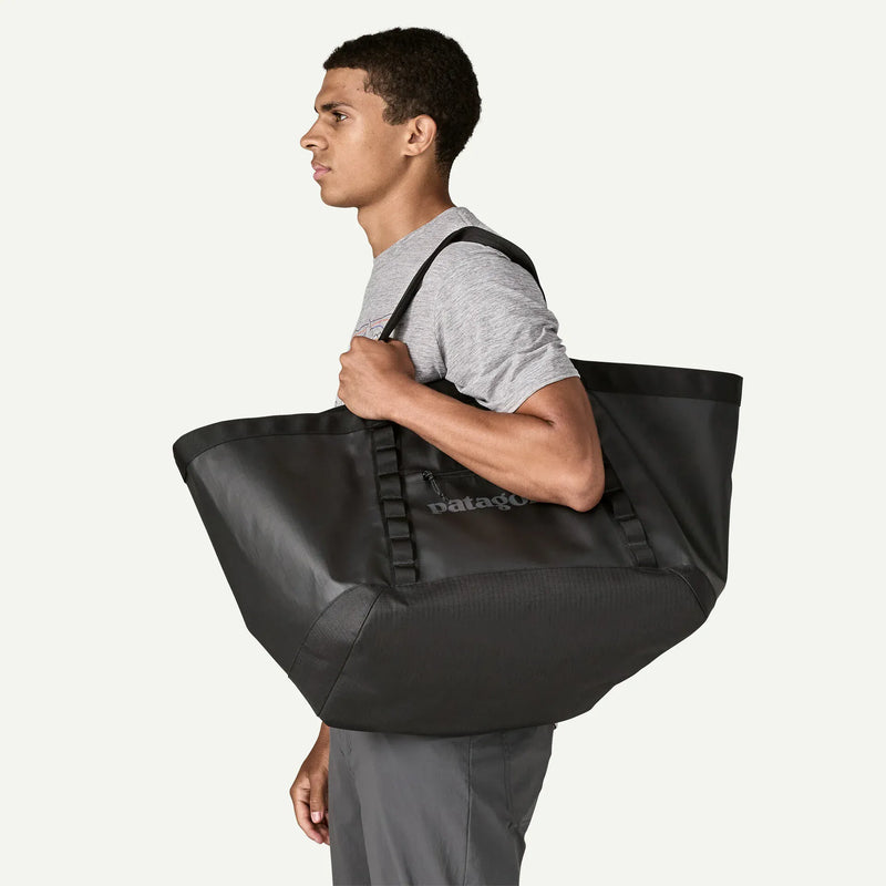 Load image into Gallery viewer, Man carrying a black tote bag with 'Patagonia' branding on a white background
