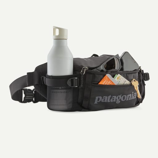 Black Patagonia waist bag with a bottle and items on a white background