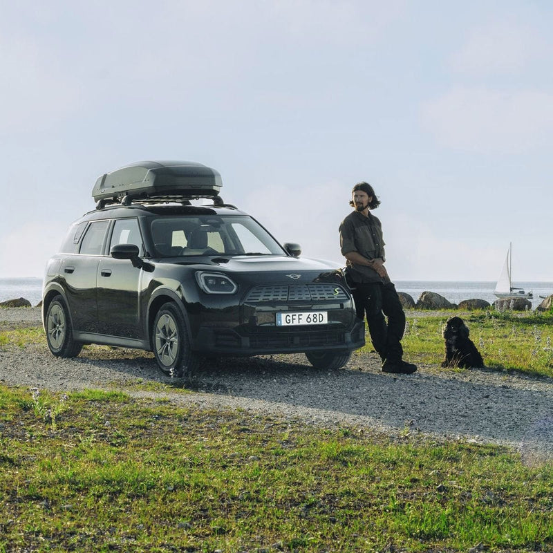 Load image into Gallery viewer, Person standing next to a car with a roof box by the seaside
