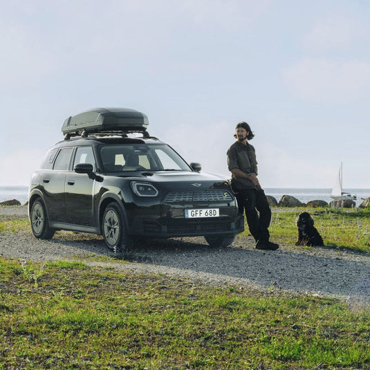 Person standing next to a car with a roof box by the seaside
