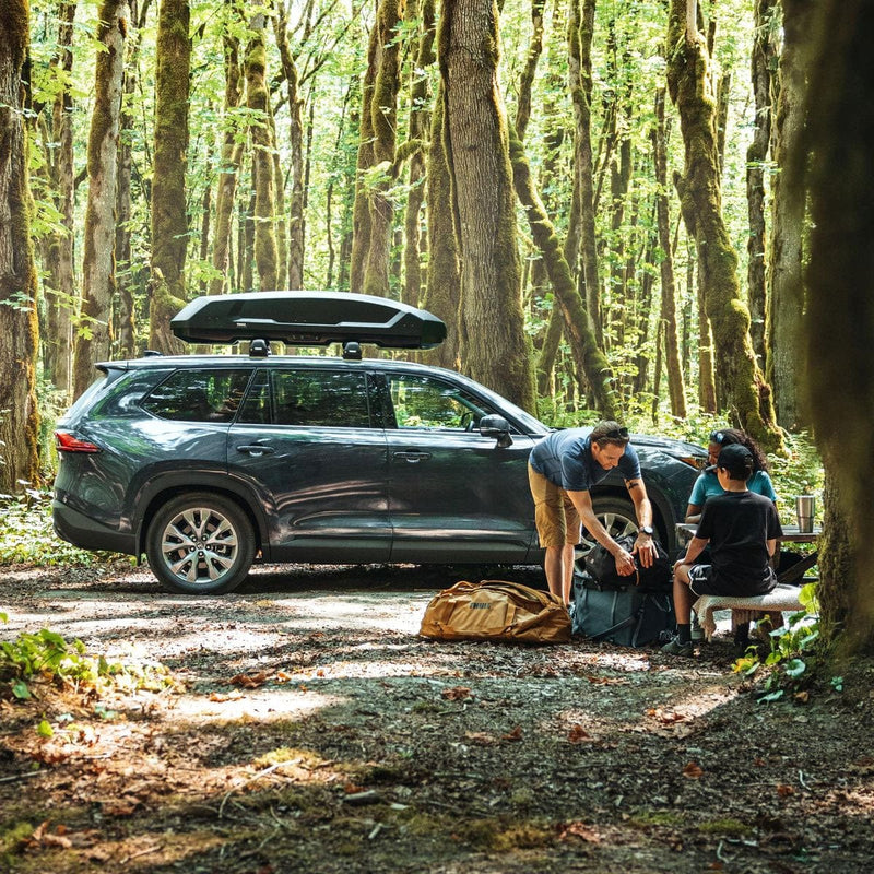 Load image into Gallery viewer, Two people preparing for a camping trip in a forest with a car and gear.
