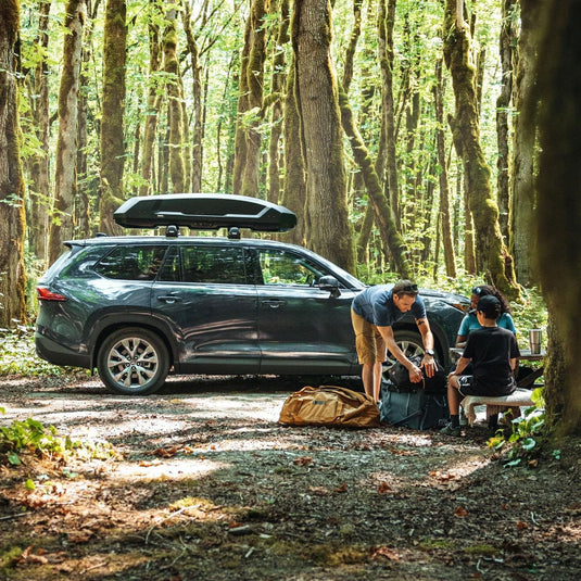 Two people preparing for a camping trip in a forest with a car and gear.