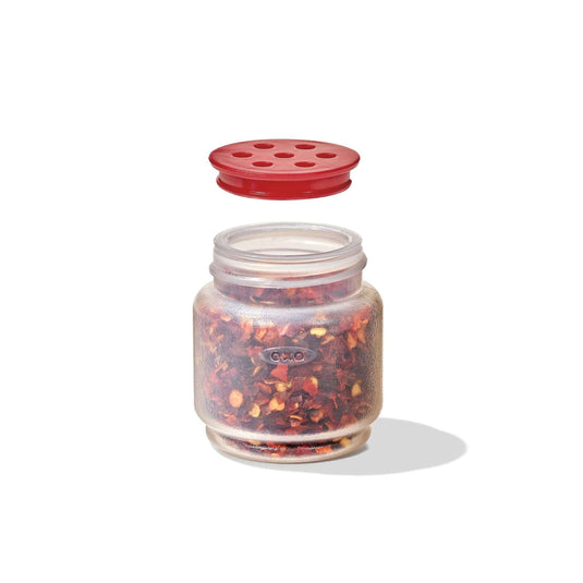 Glass jar with red lid filled with red pepper flakes on a white background