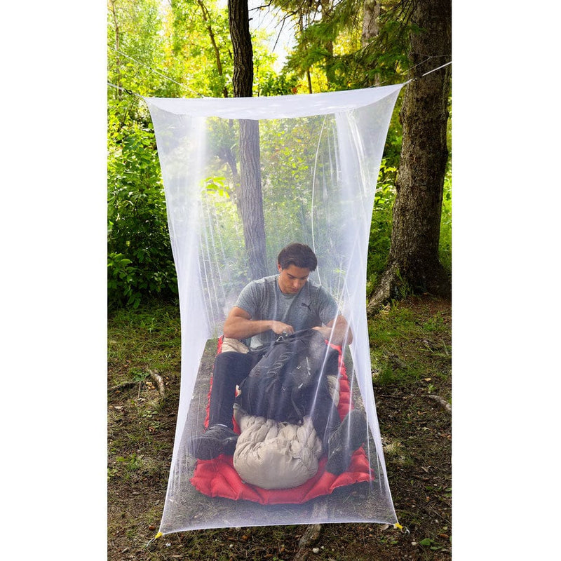 Load image into Gallery viewer, Person sitting inside a white camping mosquito net in a forest setting
