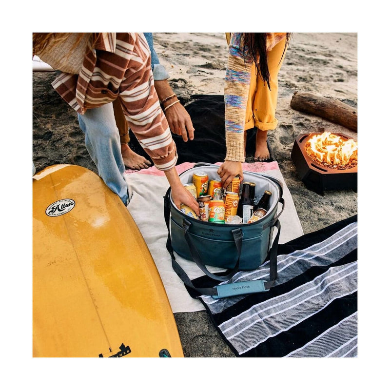 Load image into Gallery viewer, Two people by a beach with a cooler full of drinks, a surfboard, and a fire pit.
