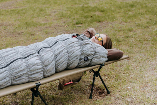 Grey goose down sleeping bag on a portable camping bed outdoors.