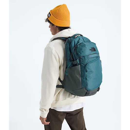 Person wearing a teal backpack with The North Face logo on a white background